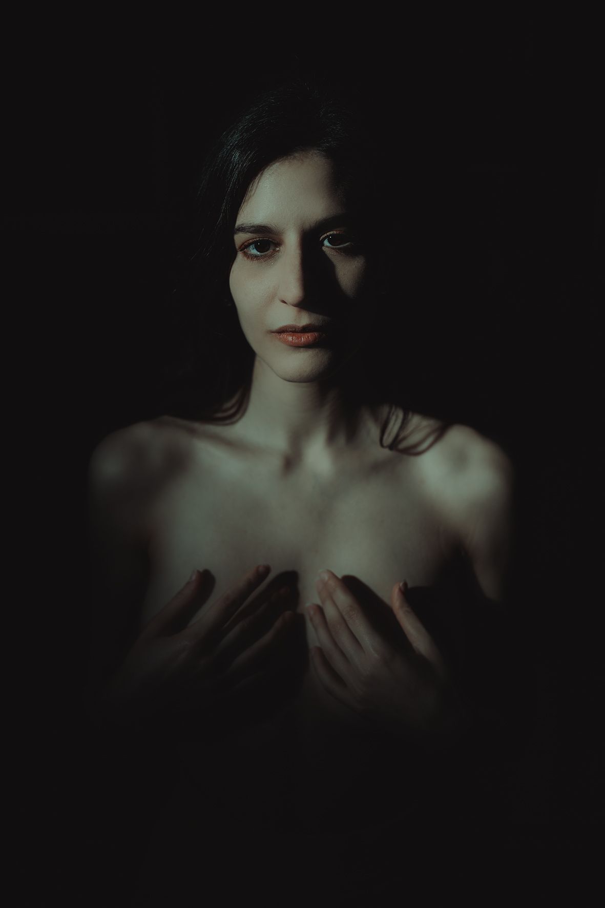 Dramatic dark portrait of a young woman with bare shoulders posed against a black background.