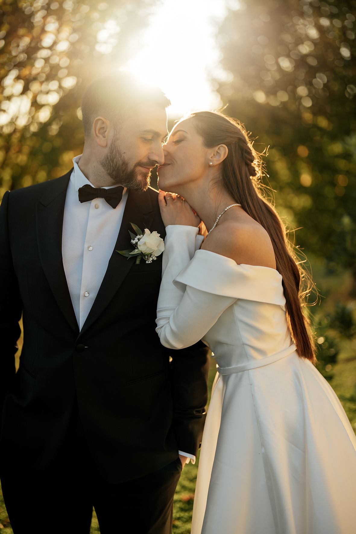 Romantic sunset wedding portrait with golden backlighting through trees.