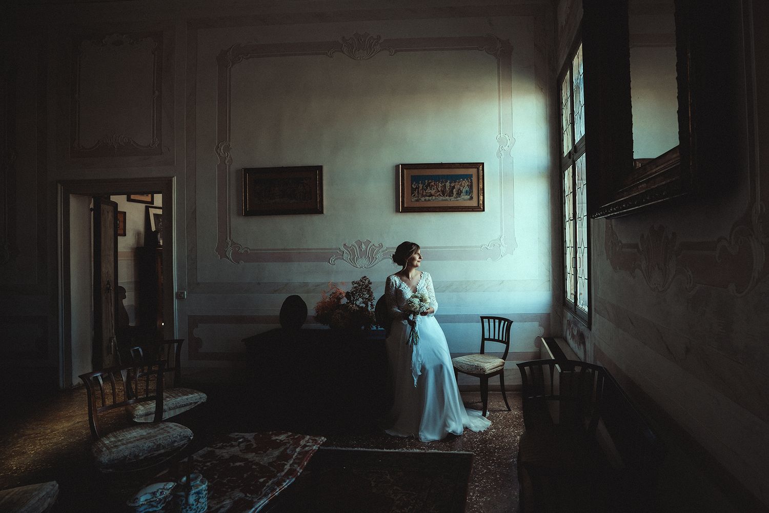 Atmospheric wedding photo of bride in vintage room with dramatic lighting.