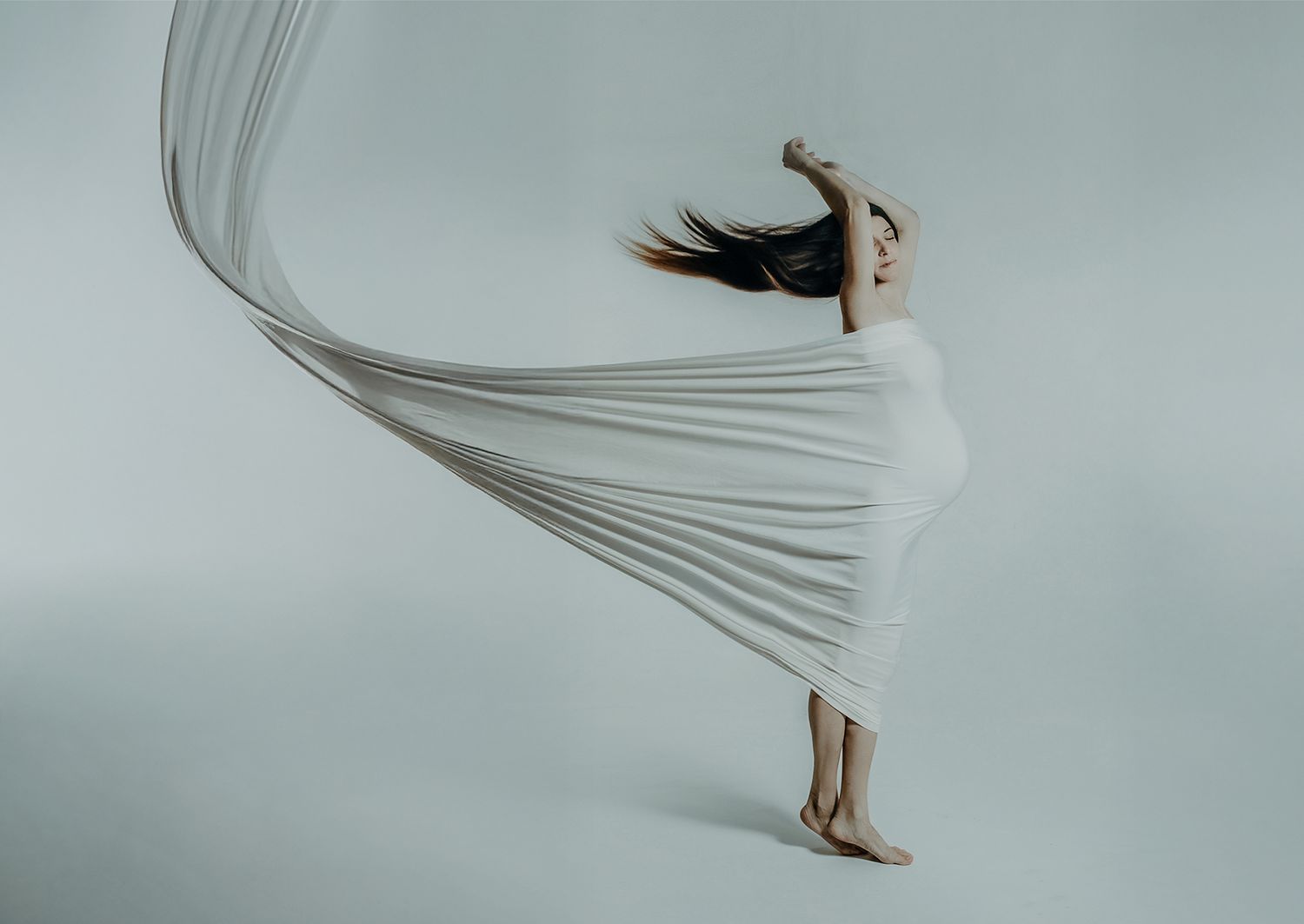 Ethereal figure study with flowing white fabric against pale background.