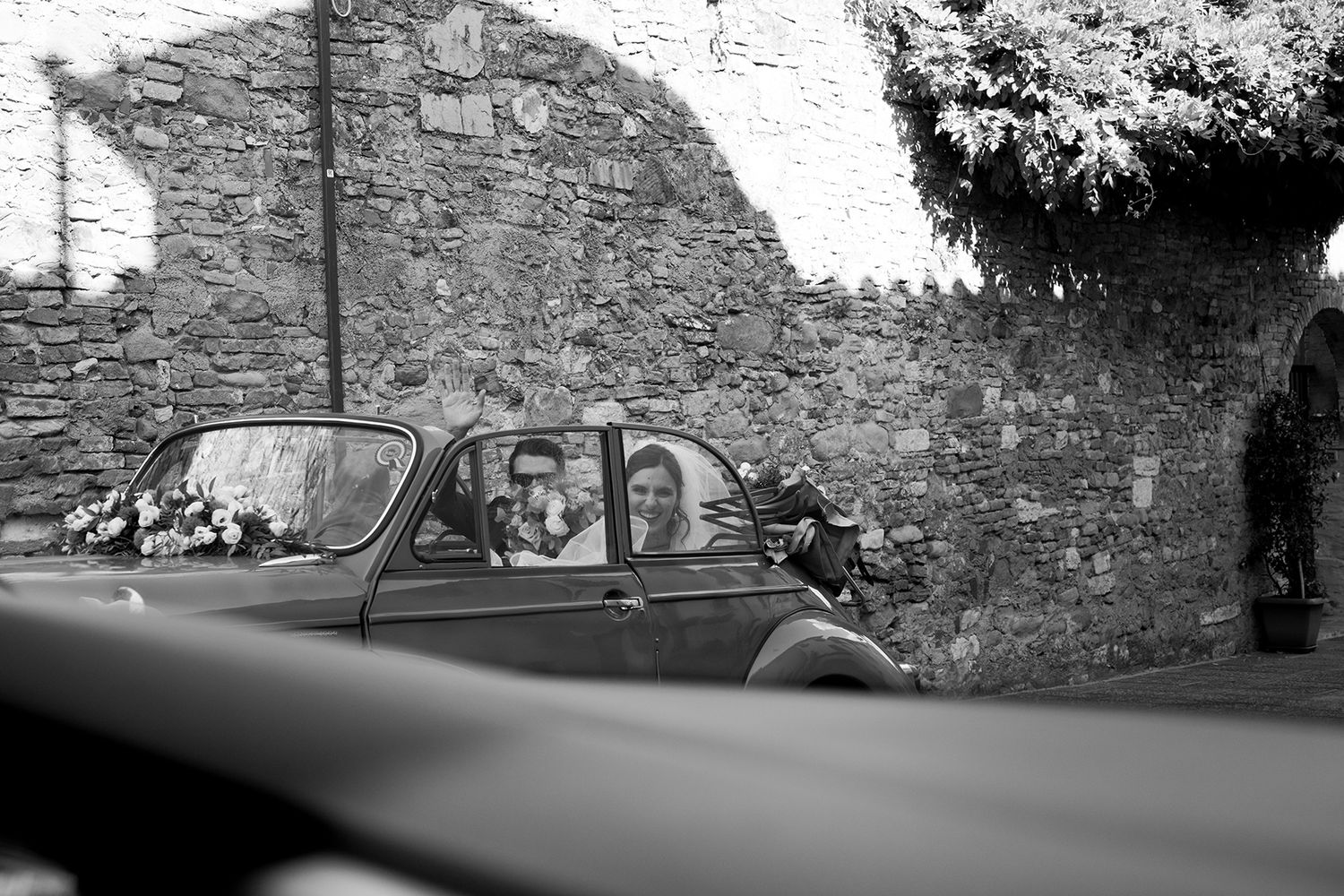 Vintage black and white photo of classic car against stone wall backdrop.