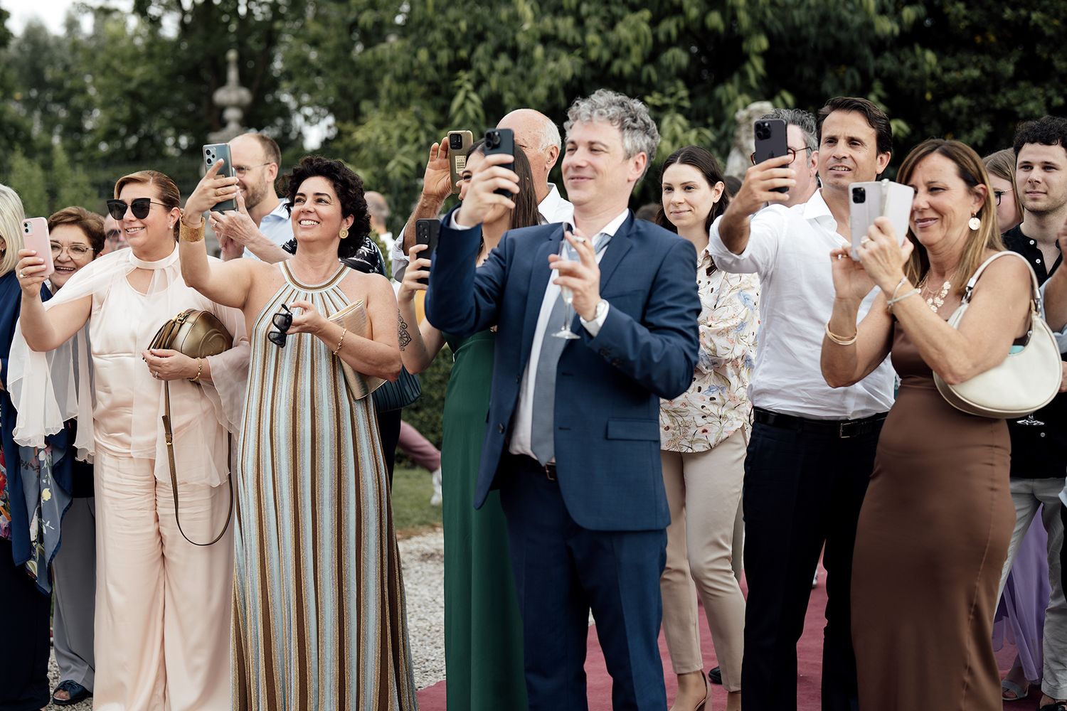 Wedding guests in neutral tones gather outside for a group celebration photo.