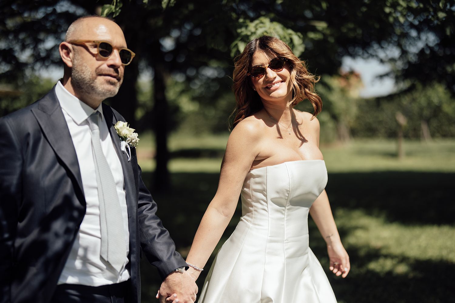 Newlyweds walking together in a sun-dappled garden setting.