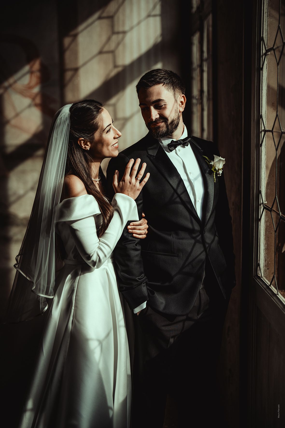 Artistic wedding portraits showing intimate moments between newlyweds near a window with dramatic lighting.
