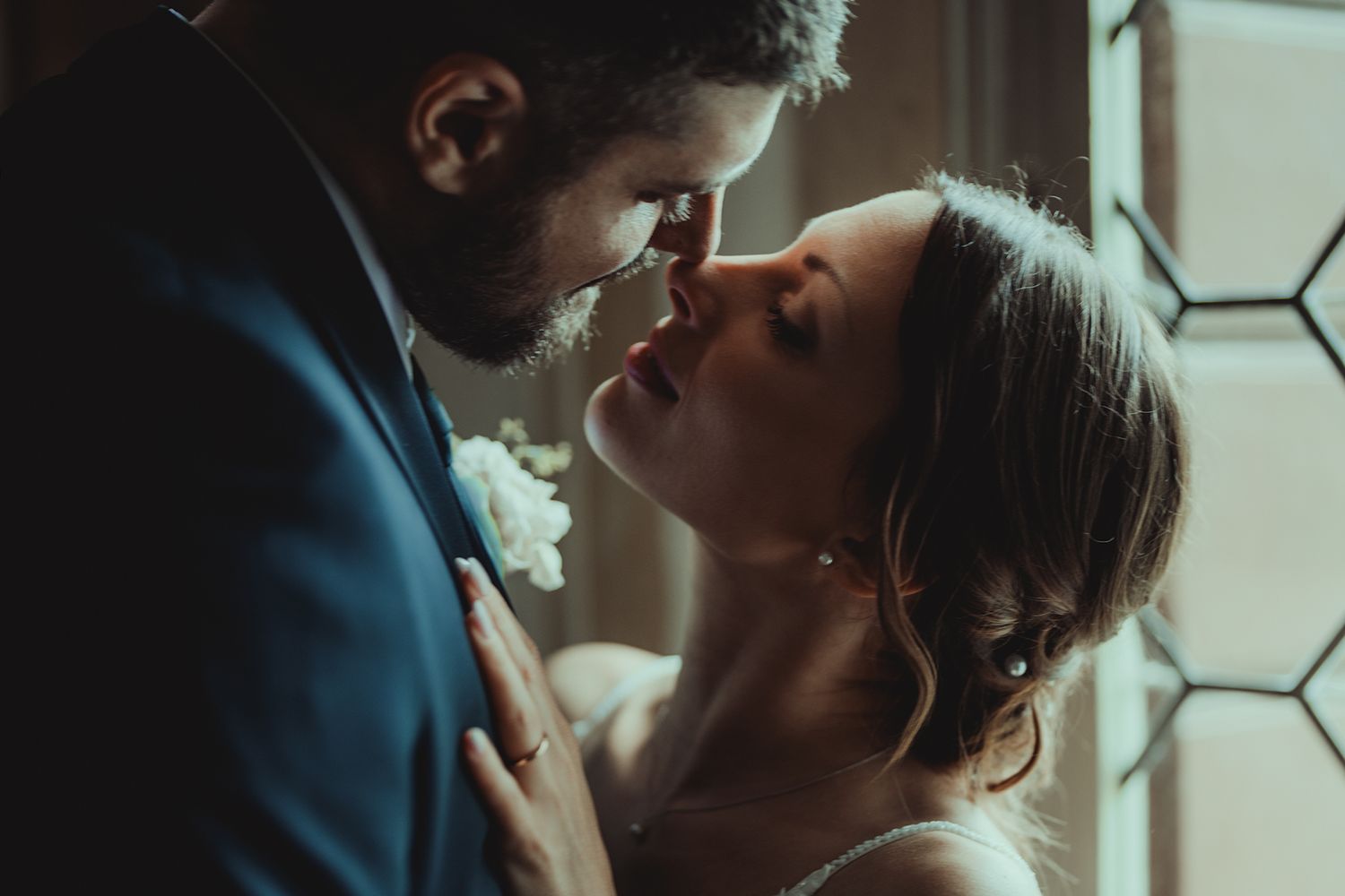 Intimate close-up of newlyweds sharing a tender moment near a window.