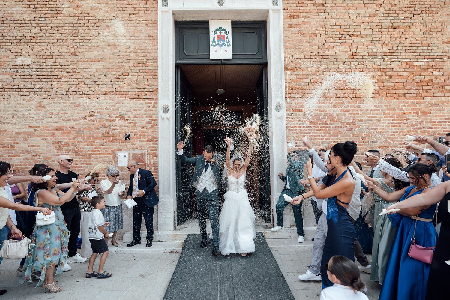 Wedding guests line up against a rustic brick wall for a celebratory photo sequence.