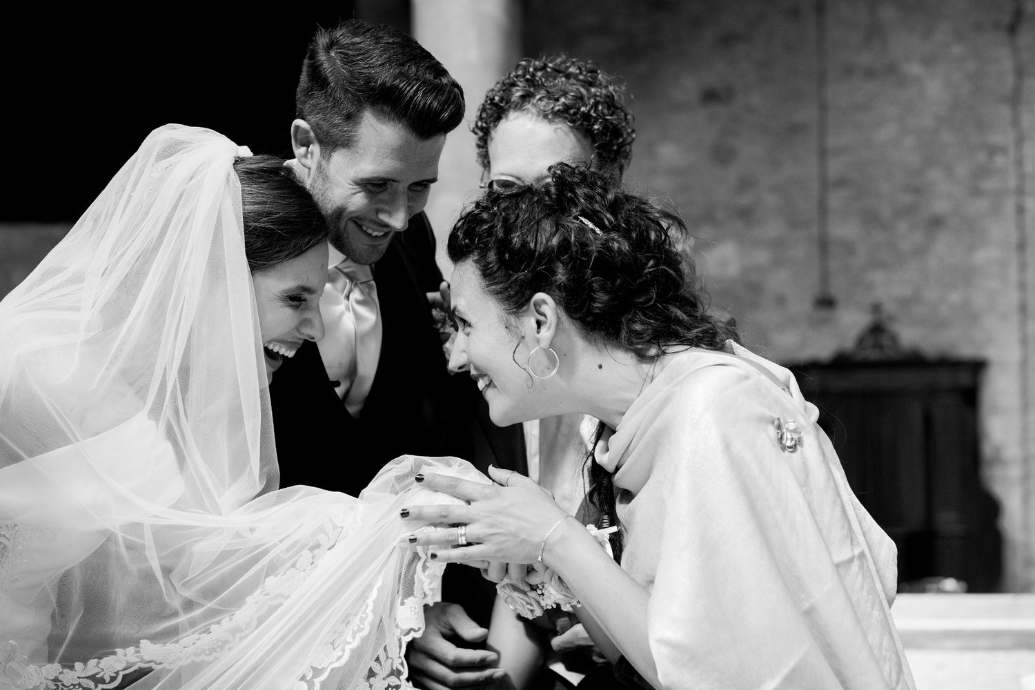 Black and white candid moment of joyful laughter between newlyweds and loved ones during wedding ceremony.