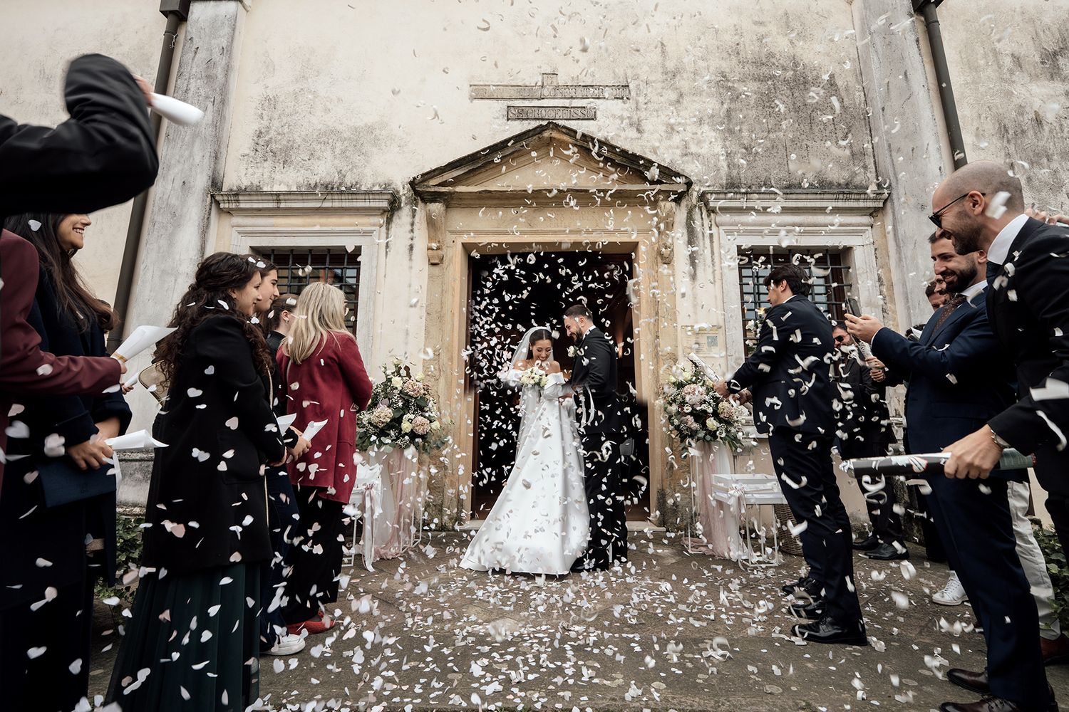Newlyweds exit church doors as guests shower them with confetti in a joyous celebration.