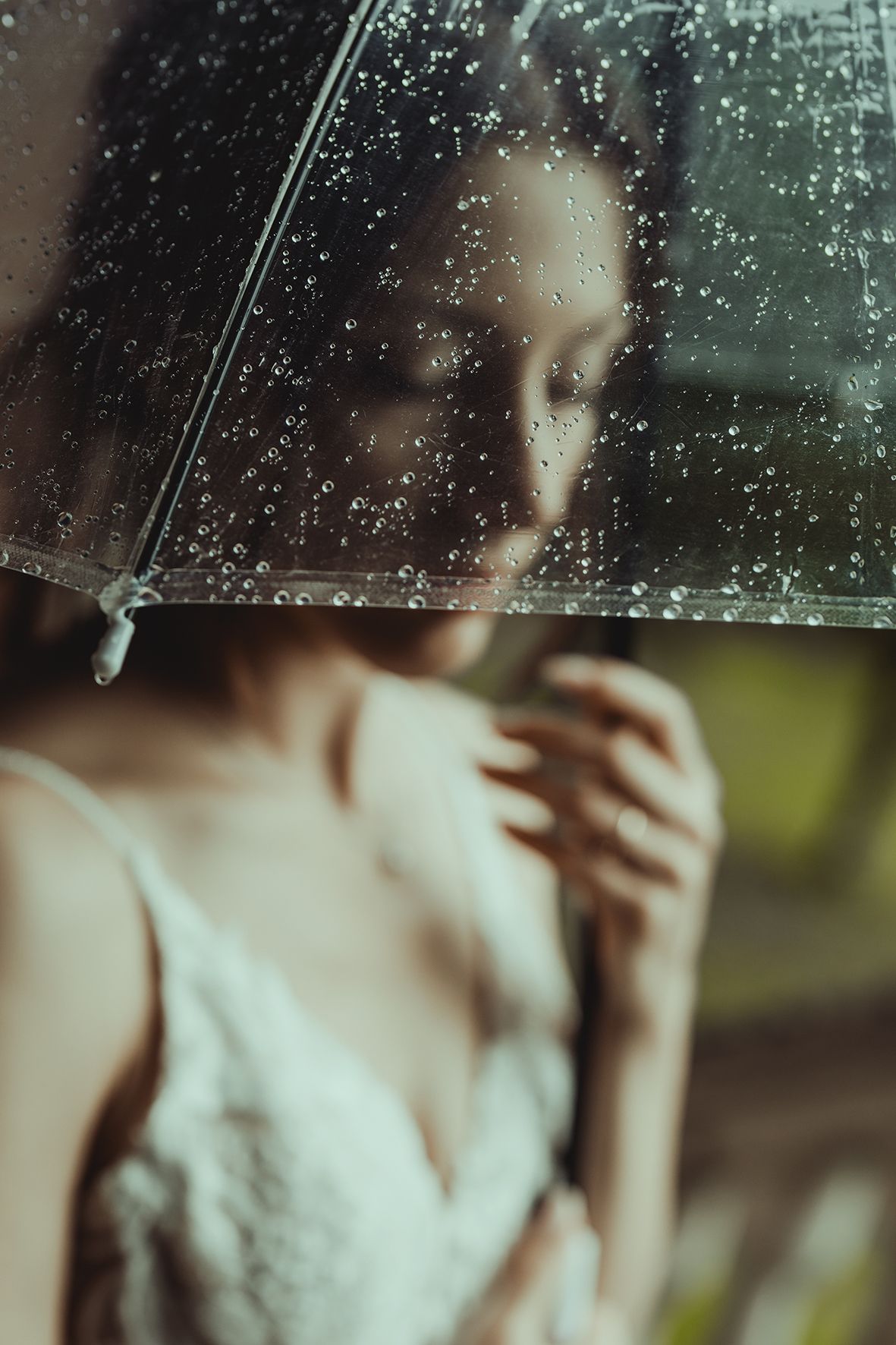 Artistic portrait through rain-covered glass showing a dreamy atmosphere with soft lighting and water droplets.