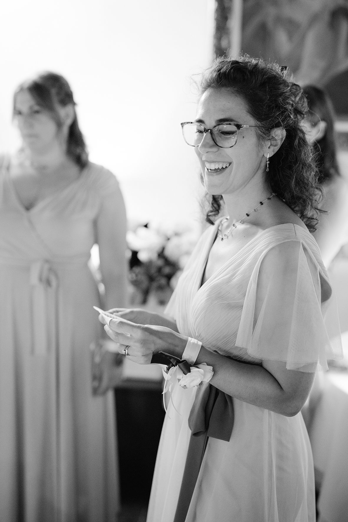 Women in light-colored dresses smiling and reacting during a wedding celebration.