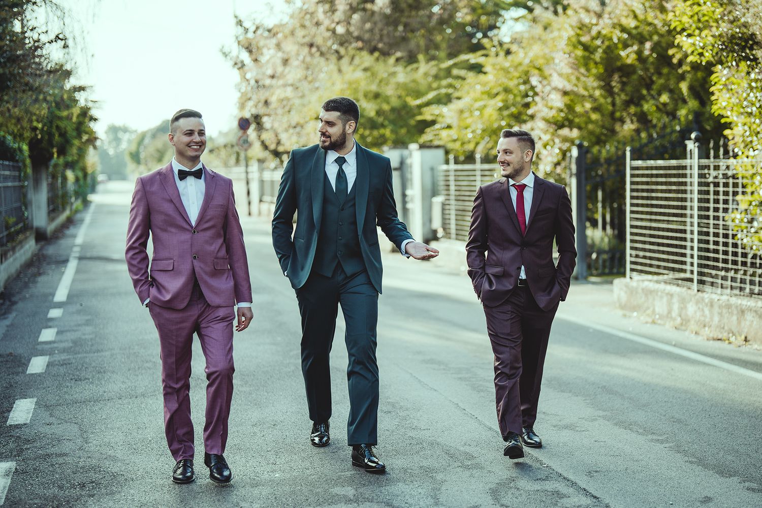 Friends in colorful suits walk together on a sunlit street.