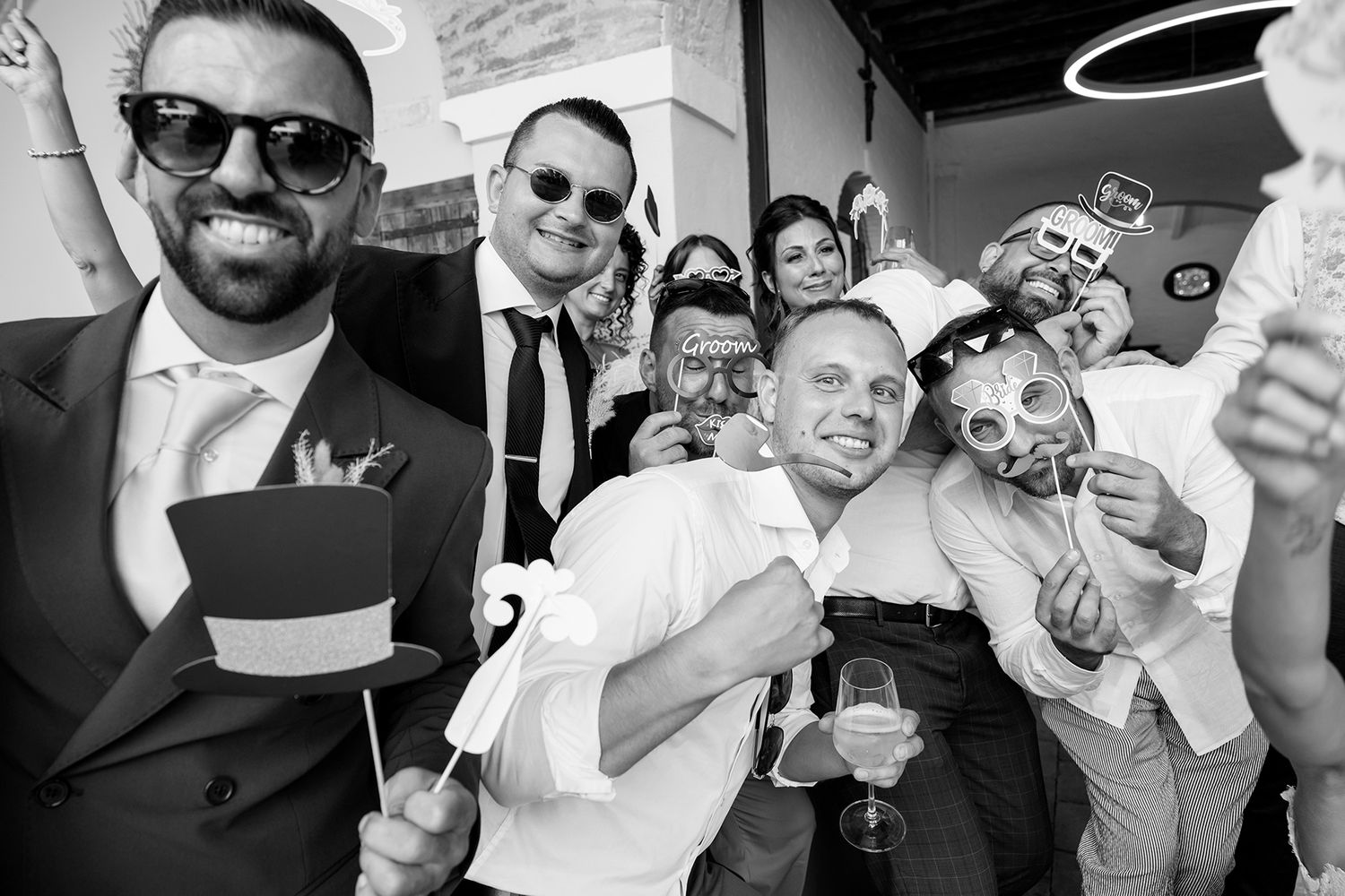 Energetic group photo of wedding guests posing with props and sunglasses at reception.
