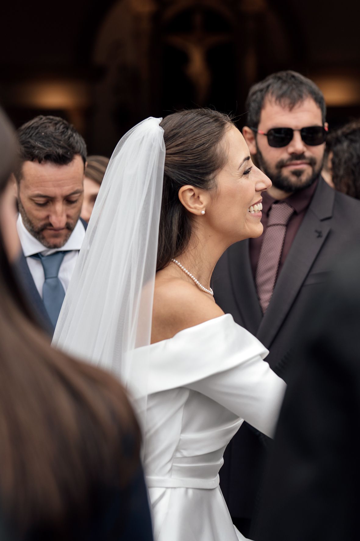 A radiant bride in an off-shoulder white gown smiles during her wedding celebration.