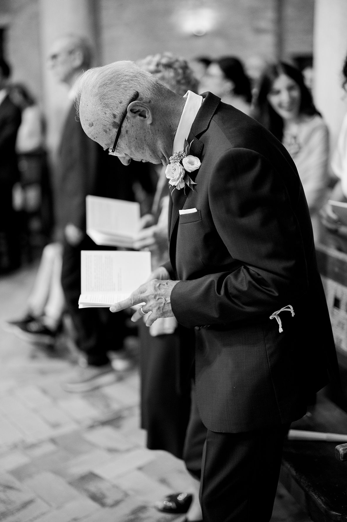Elderly man in formal attire bowing head during church ceremony.