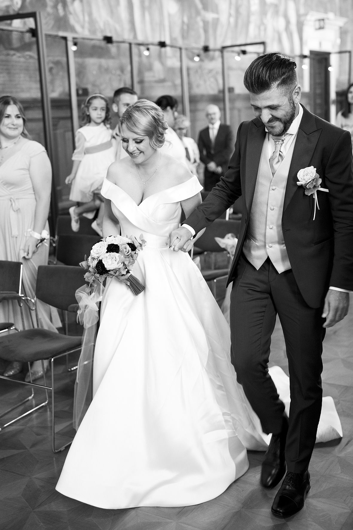 Wedding couple walking together in formal attire captured in black and white.