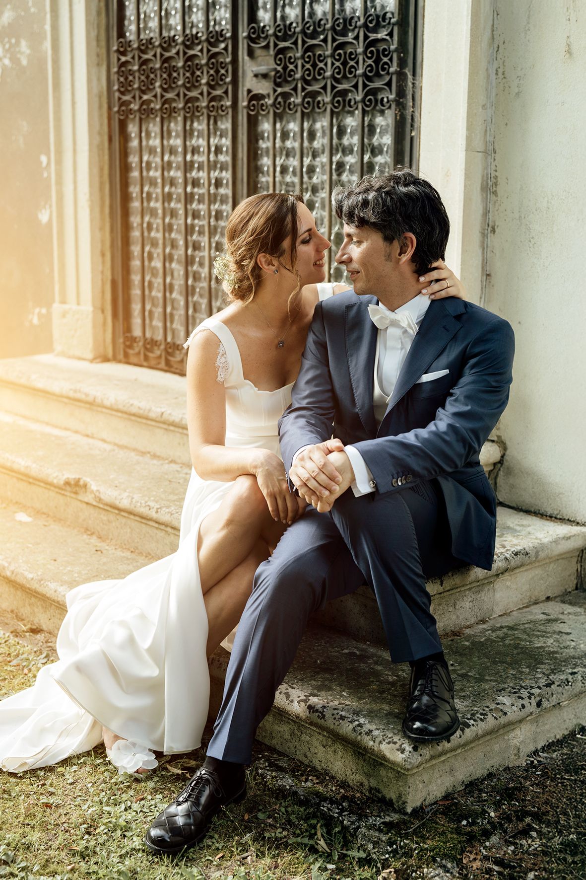 Romantic couple sitting together on stone steps in wedding attire during golden hour.