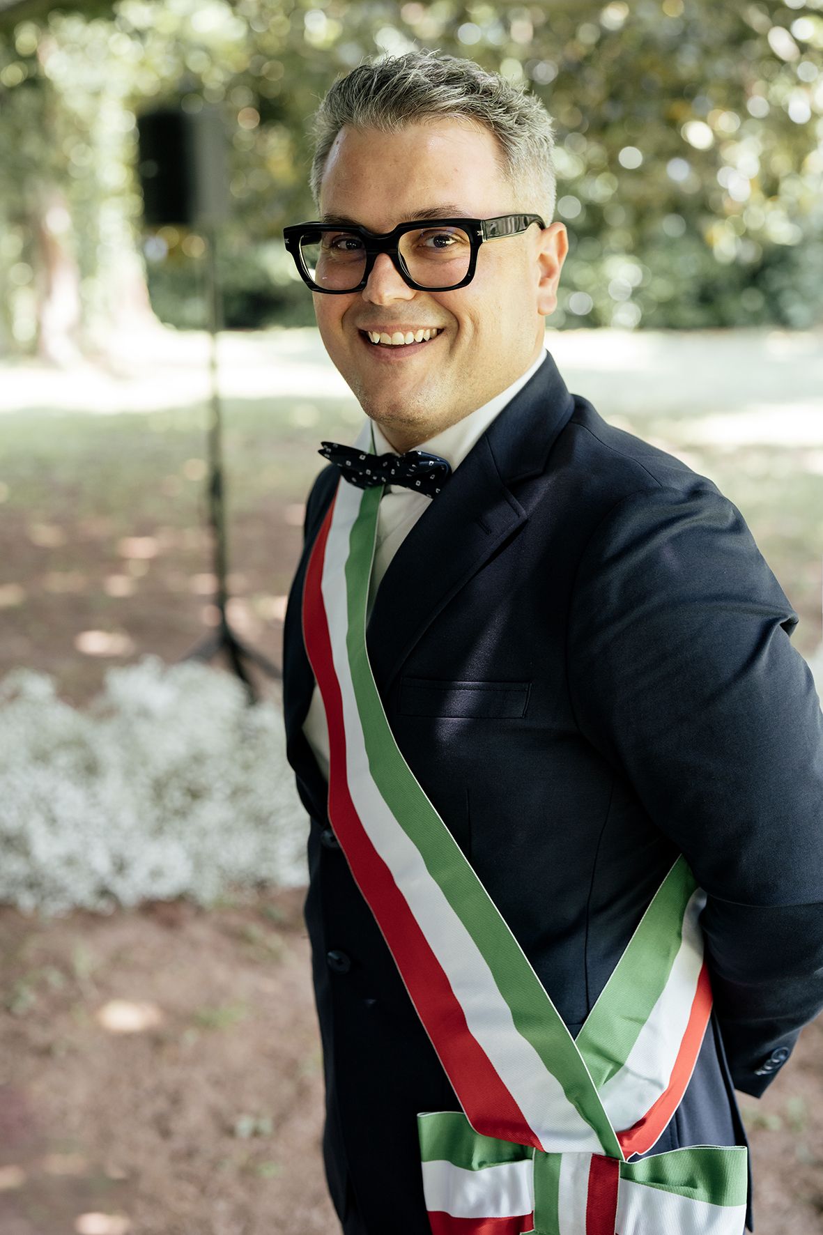 An official wearing glasses and a tricolor sash smiling at the camera.