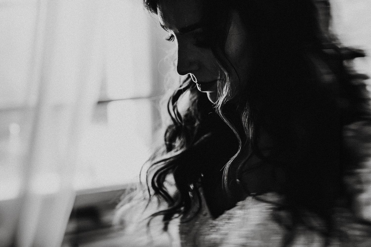 Black and white profile portrait of a woman with long wavy dark hair, captured in soft artistic blur.
