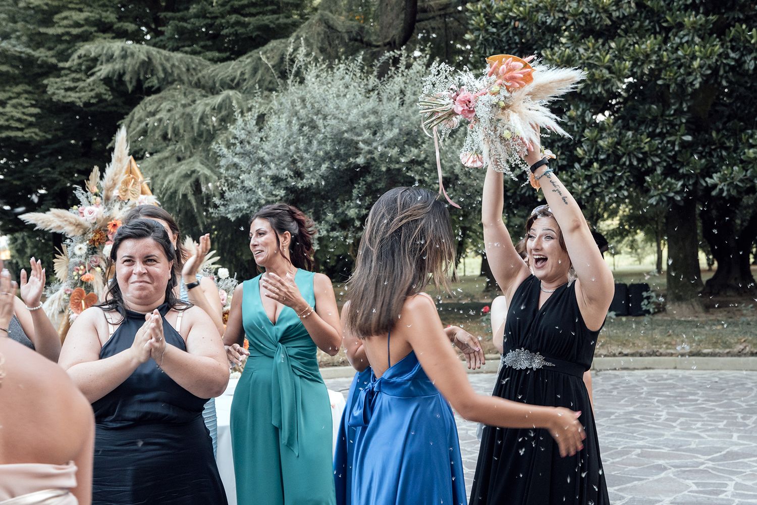 Wedding celebration with guests dancing in formal attire and colorful dresses outdoors.