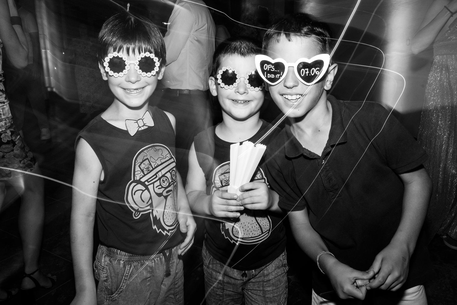 Group of party attendees posing together wearing sunglasses in black and white.