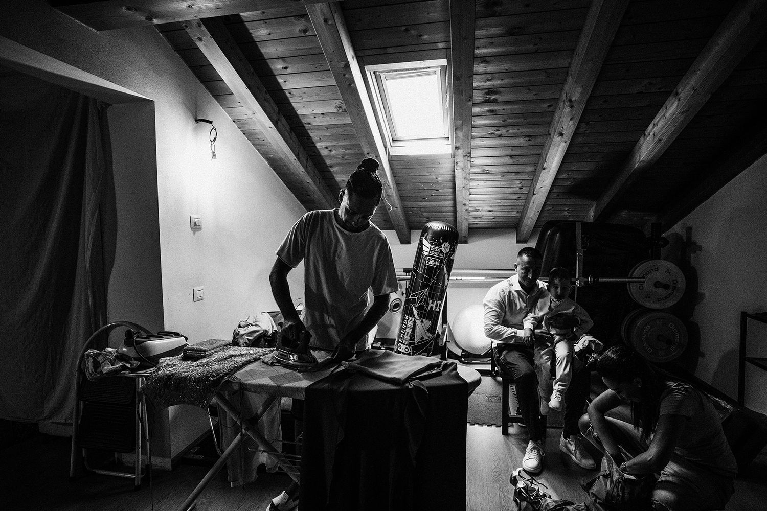 Black and white photo of two men in a dimly lit attic room with wooden ceiling and skylight.