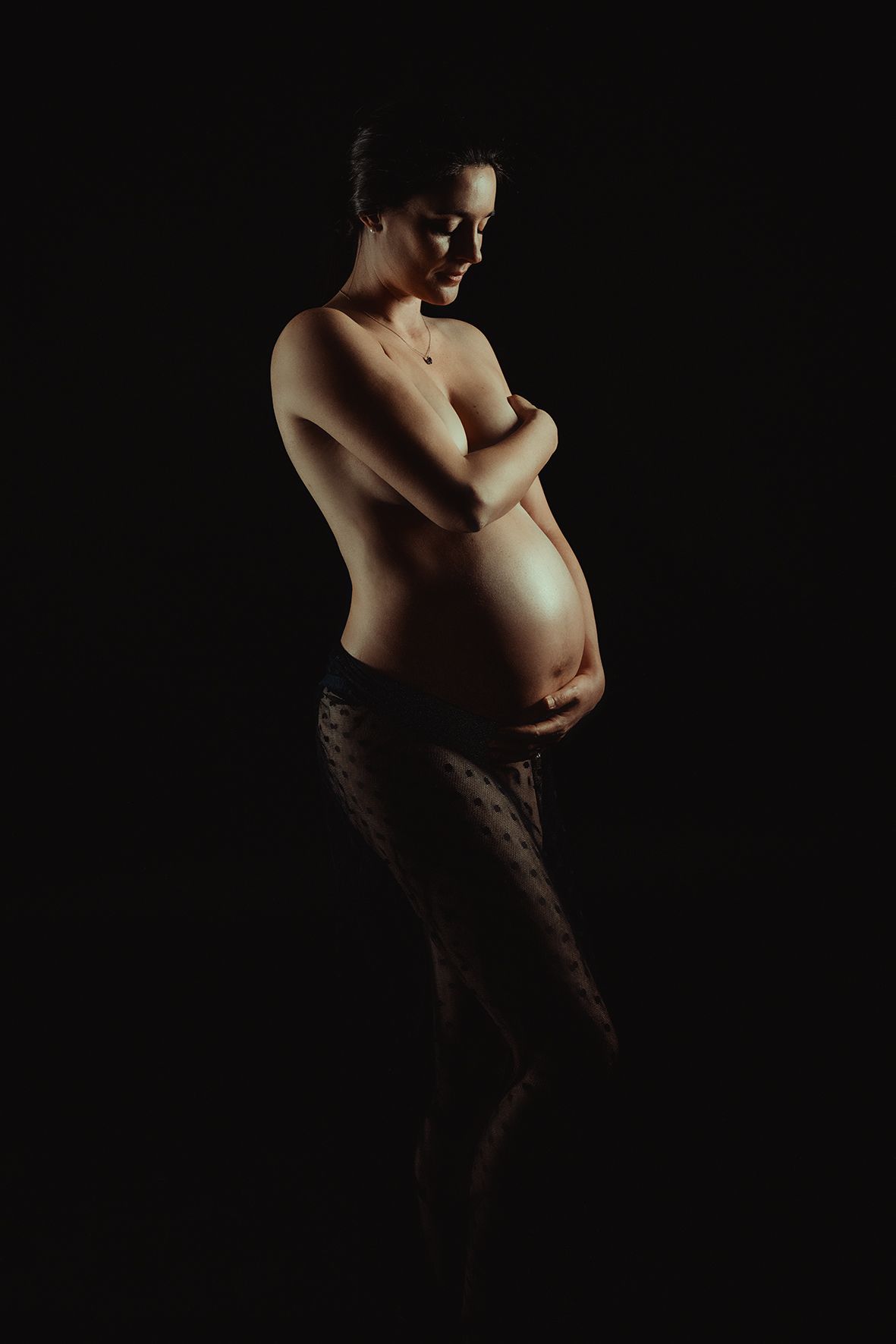 Dramatic low-key nude study with selective lighting in dark setting.