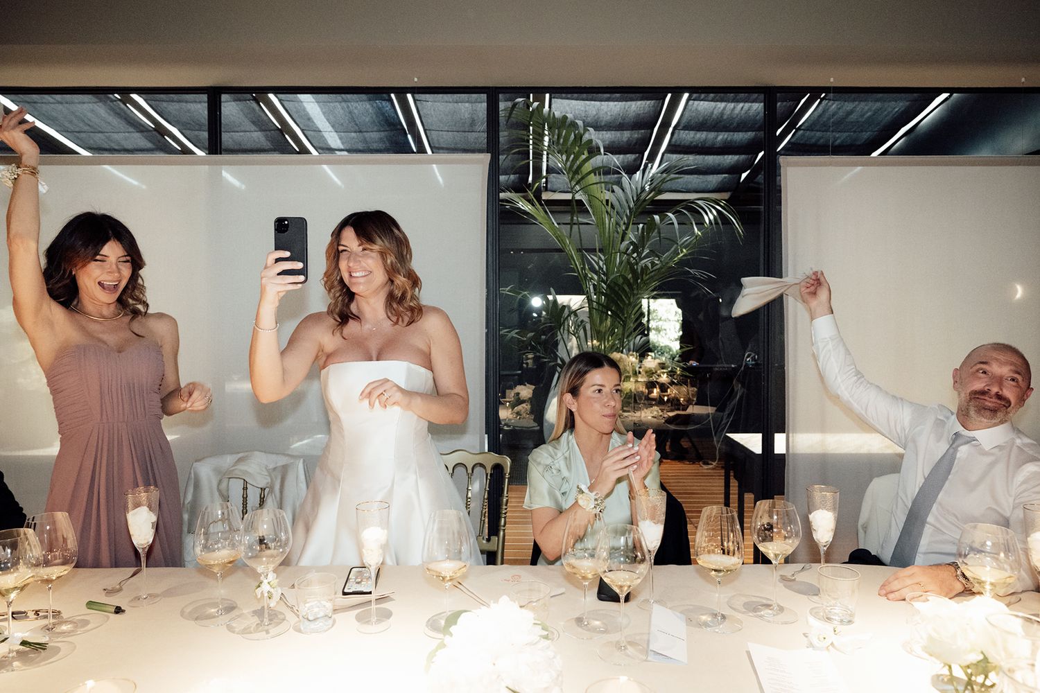 Wedding reception guests celebrate with raised napkins in candid moments.
