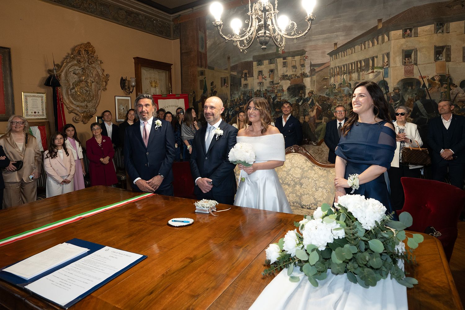 An elegant wedding ceremony in a grand room with chandeliers and ornate decor.