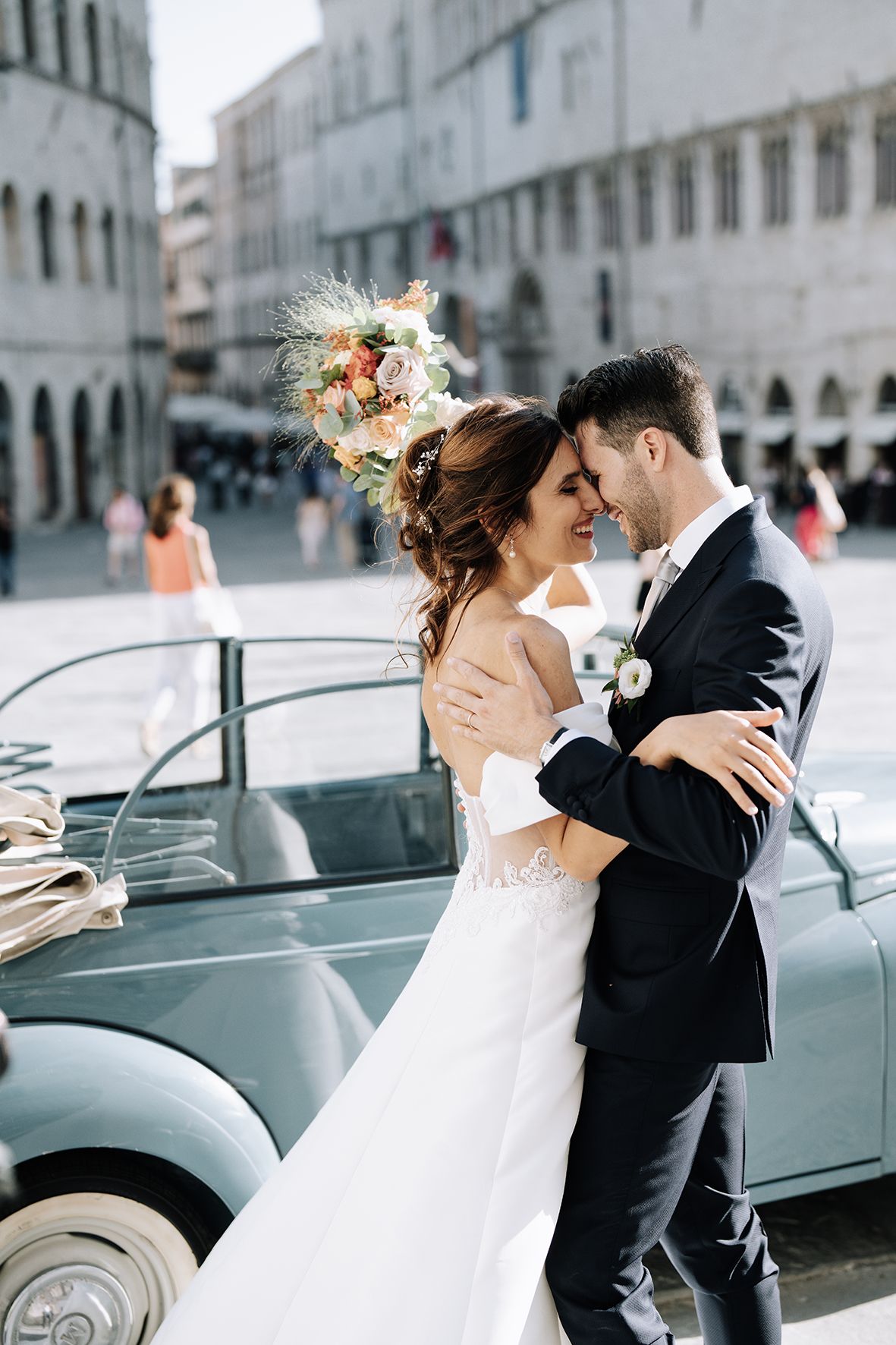 Romantic wedding sequence showing couple embracing near vintage cars on a European street.