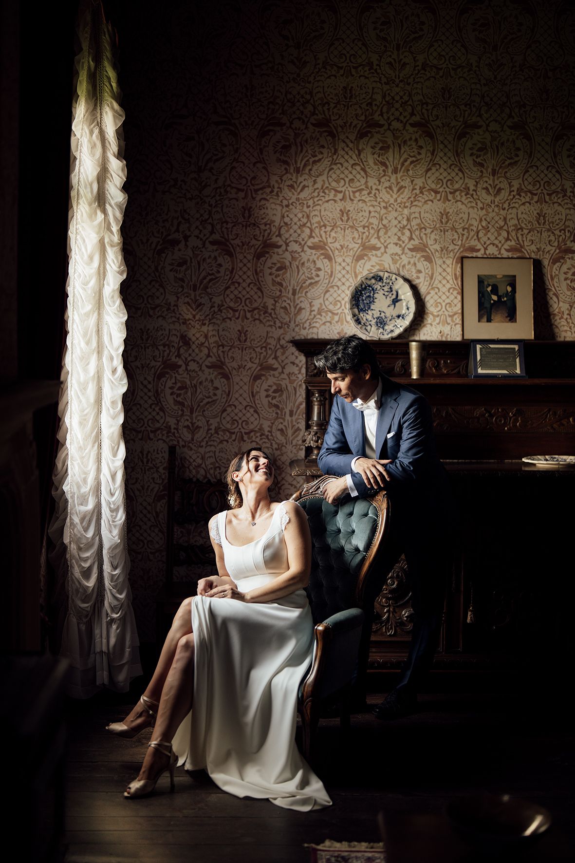 Dramatic lighting illuminates a vintage room with piano and elegant furnishings.