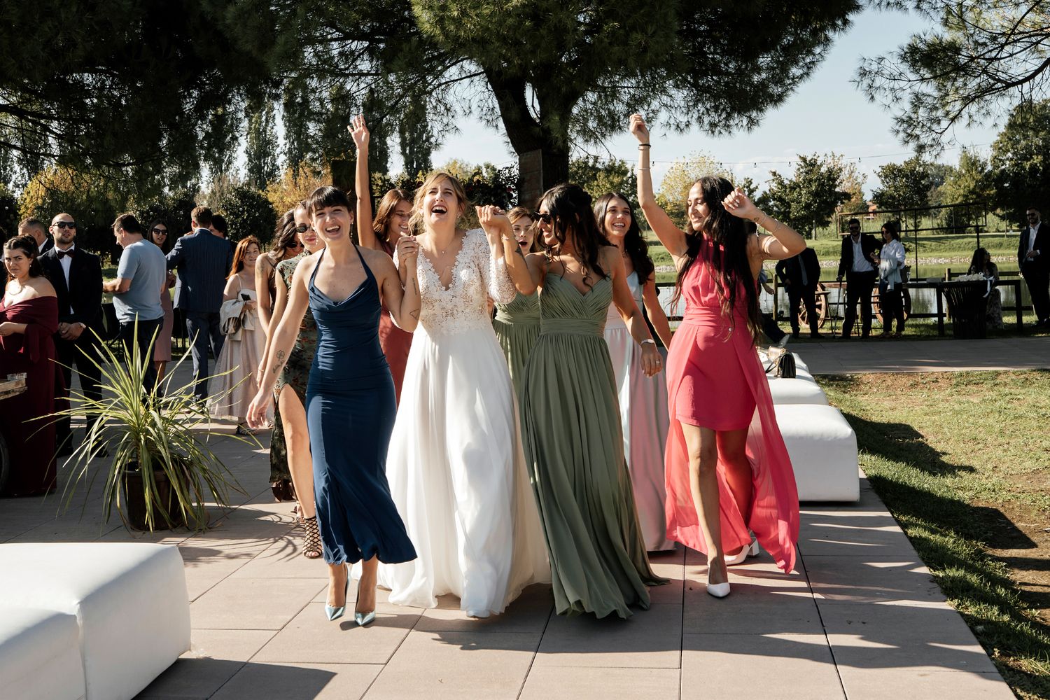 Wedding guests gather outside on a sunny day wearing colorful dresses.
