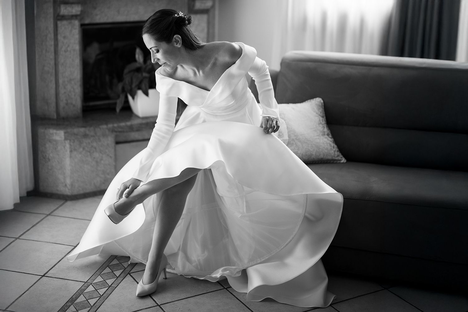 Bride in flowing white wedding dress twirls gracefully on tiled floor in black and white photograph.