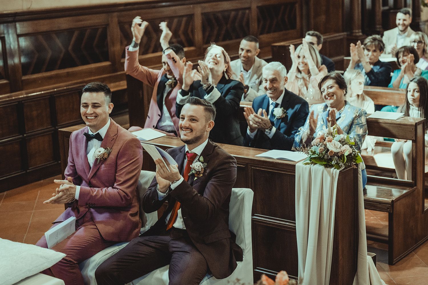 Joyful wedding guests celebrate and cheer from church pews during the ceremony.
