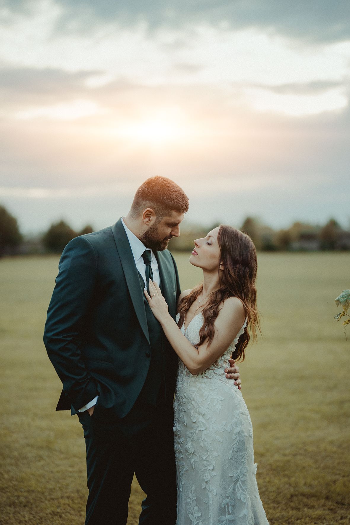 A romantic sunset photoshoot in an open field with dramatic cloudy sky backdrop.