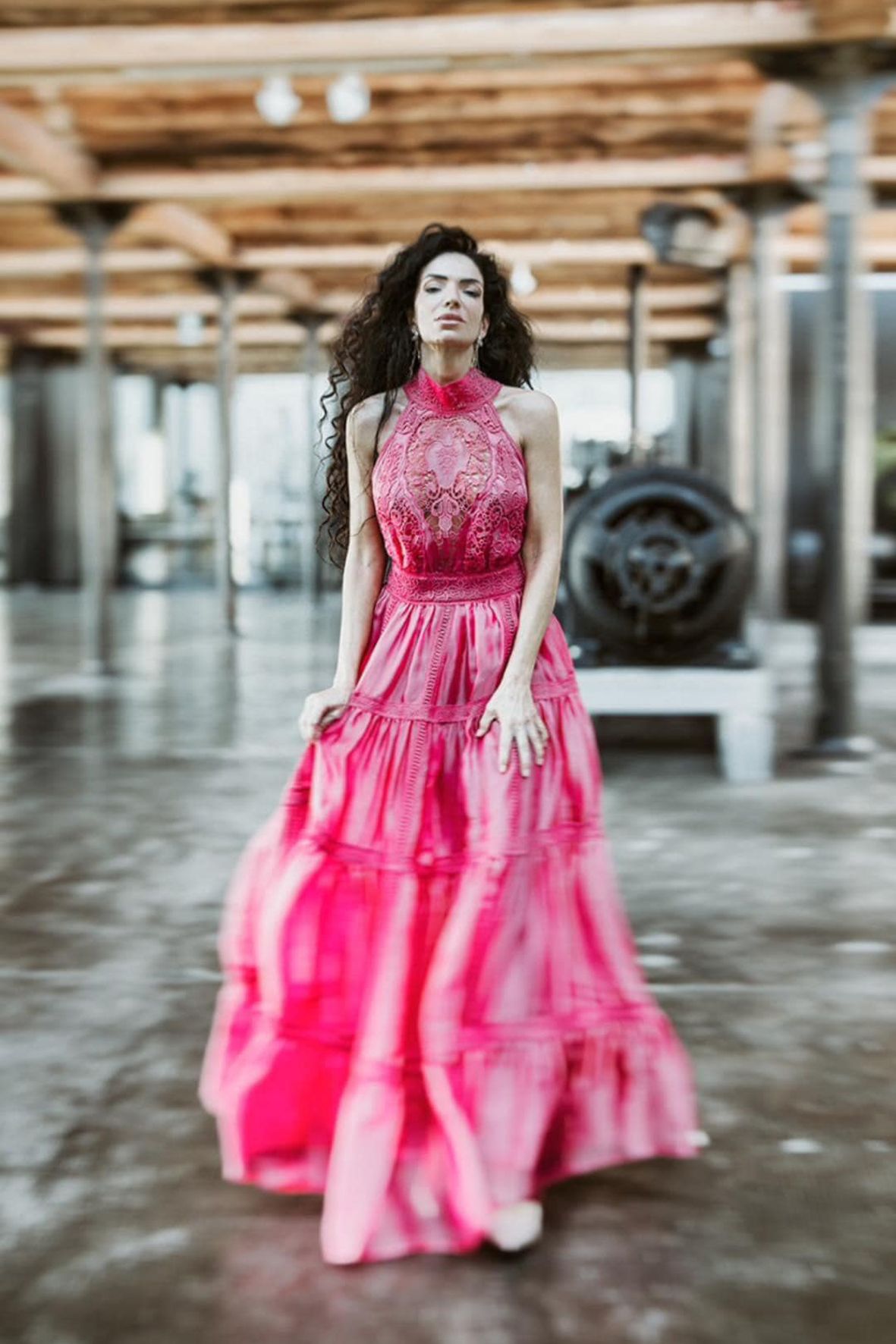 Figure in bright pink dress twirling in an industrial space with wooden beams.