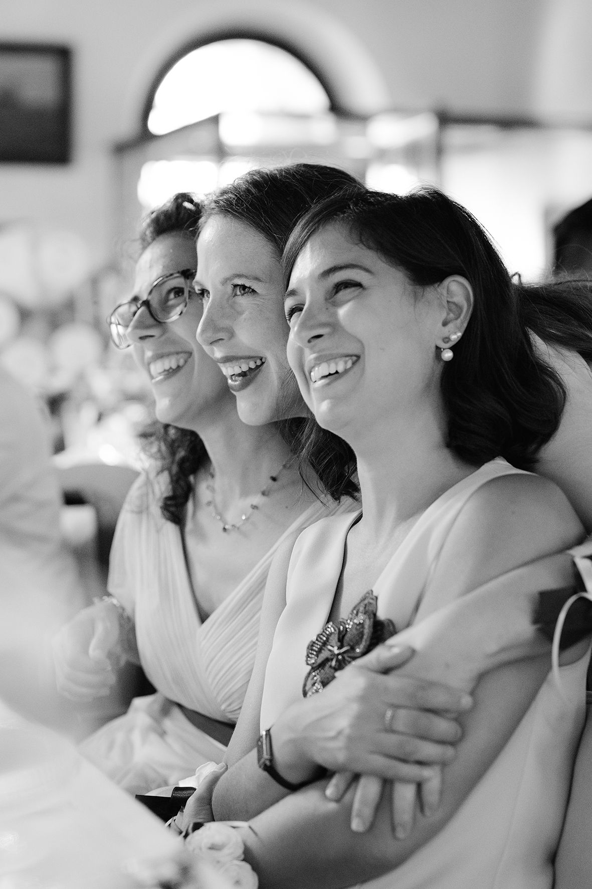 Group of wedding guests sharing laughter and embraces in black and white photography.