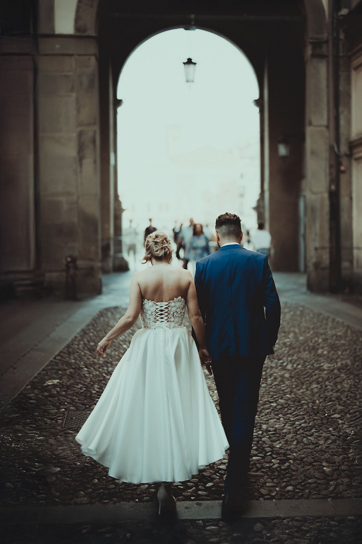 A couple in wedding attire walking through an arched passageway.