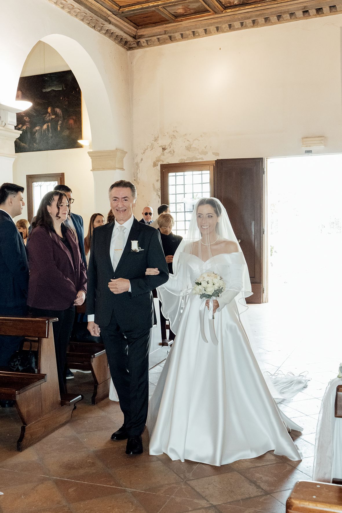 Wedding party gathering inside historic church with ornate wooden ceiling and white walls.