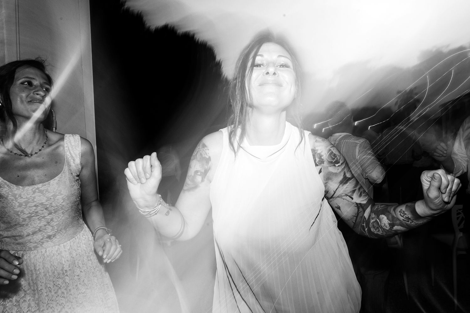 Black and white photo of wedding guests dancing and celebrating with dramatic lighting.