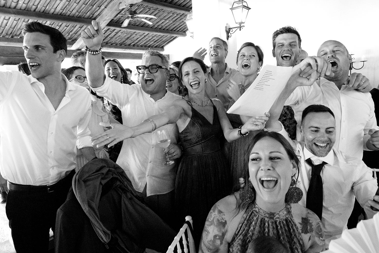 Wedding guests celebrate with joyful expressions and raised arms during a festive reception moment.