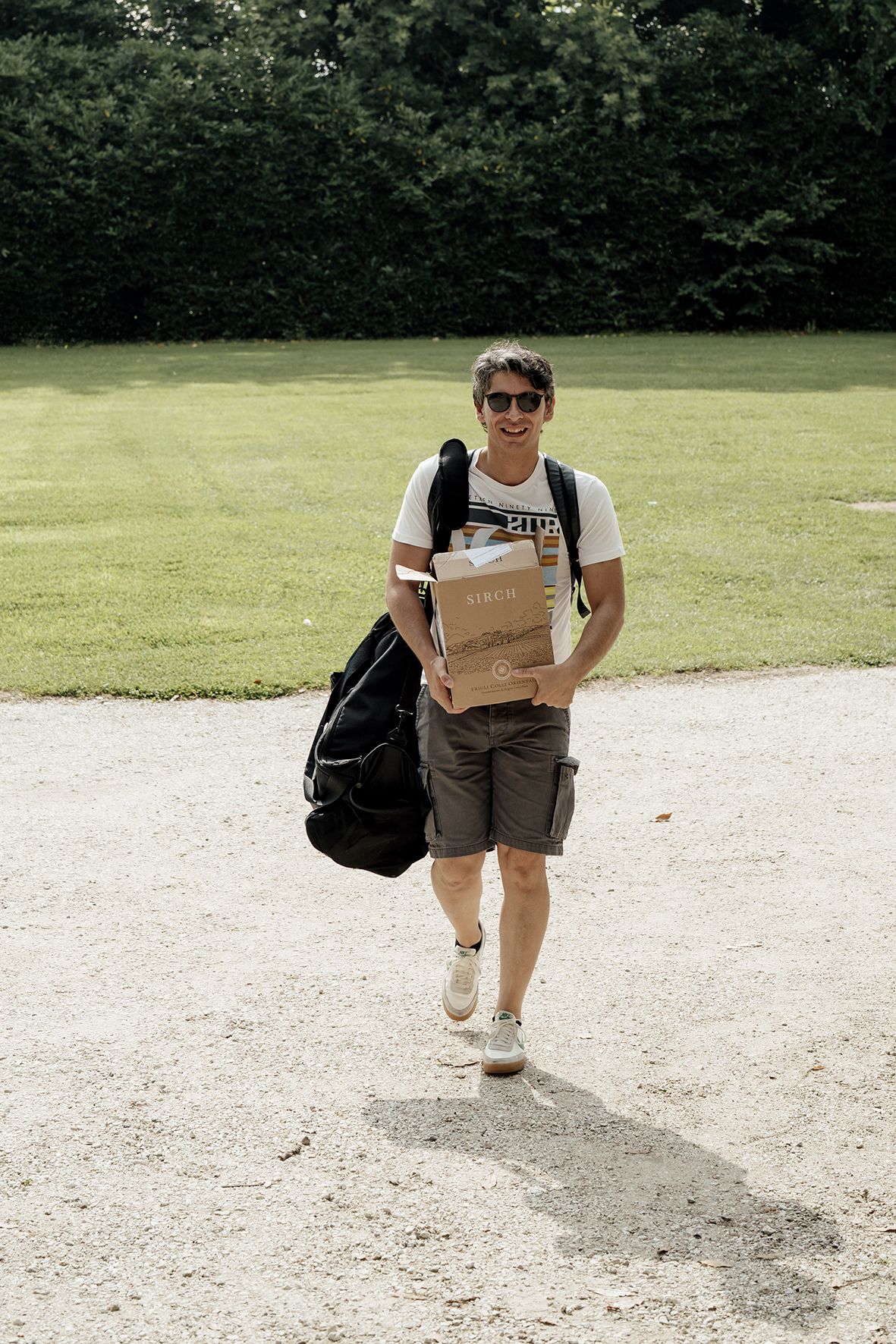 Person walking on path carrying shopping bag and backpack.