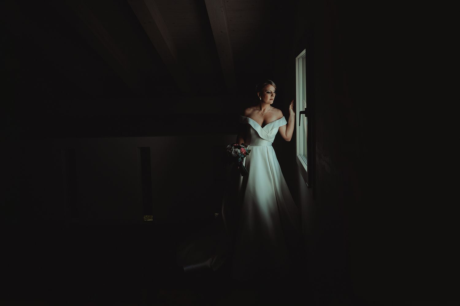 Dramatic silhouette of bride in white gown standing in doorway.