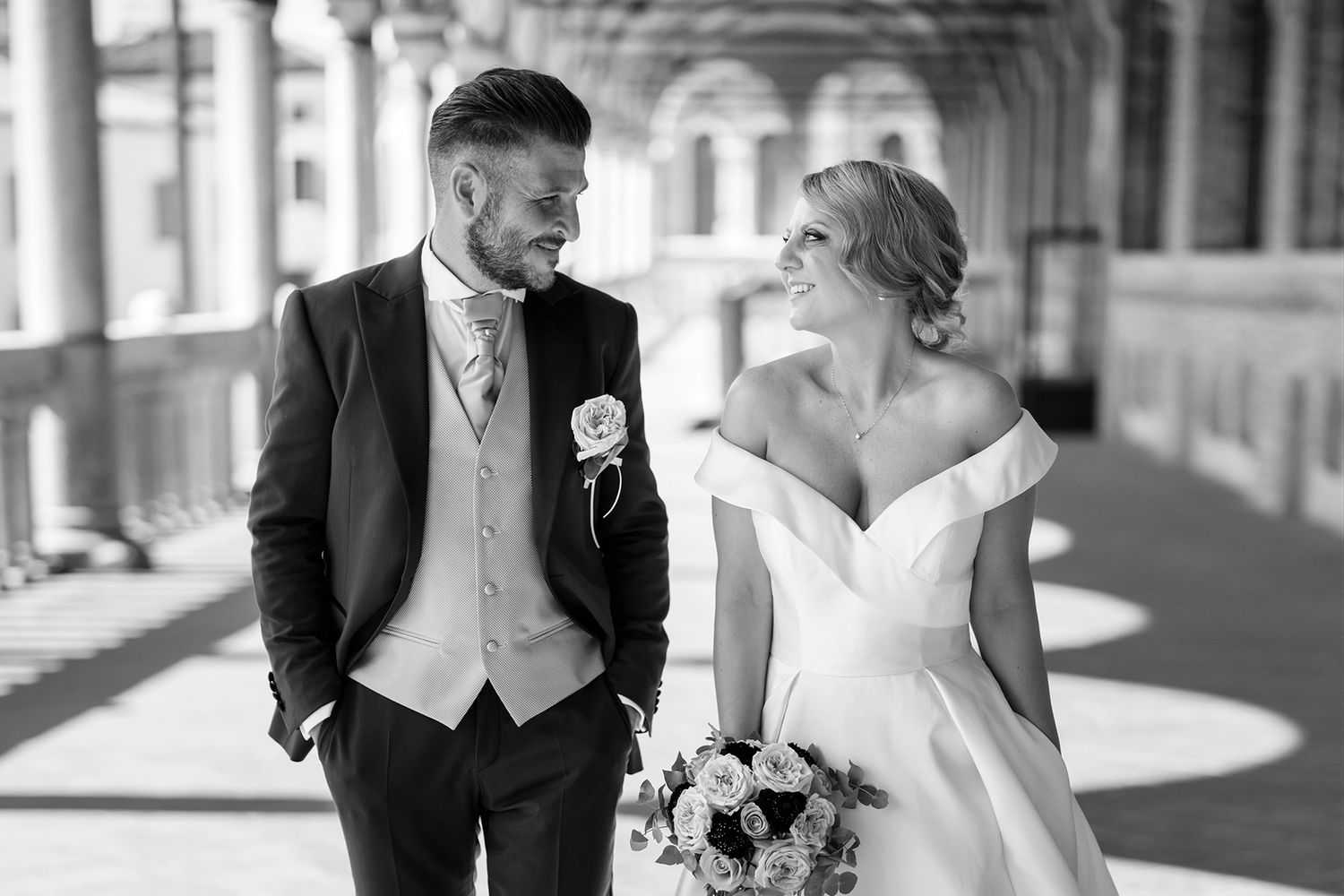 Elegant wedding couple posing together in a historic colonnade setting.