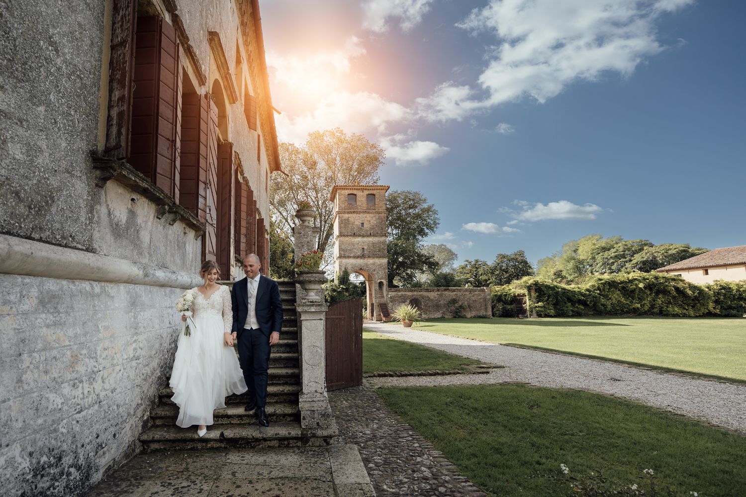 Wedding couple descends stone steps of historic building in golden sunlight.