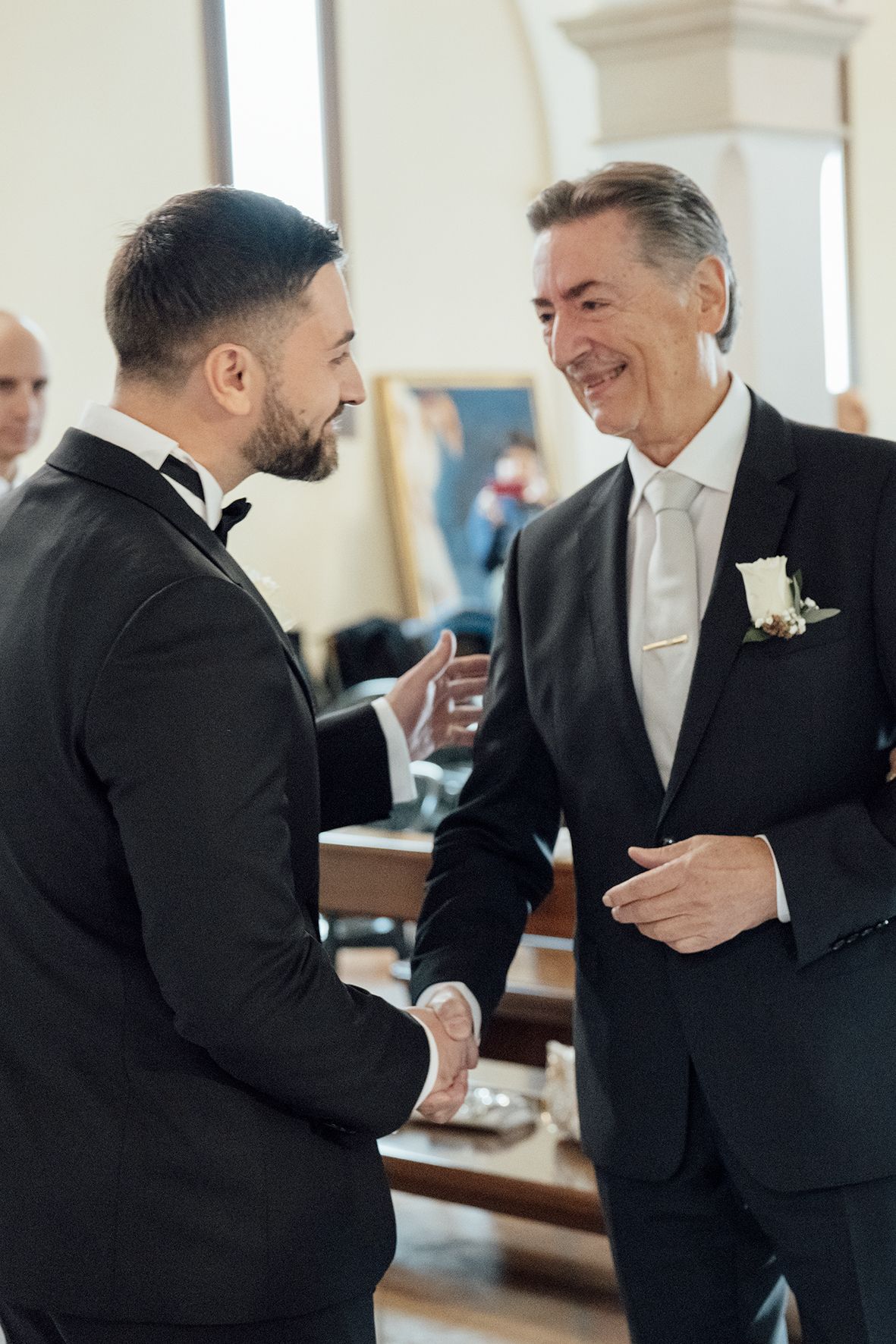 Wedding guests and groomsmen sharing laughs and conversation in formal church setting.