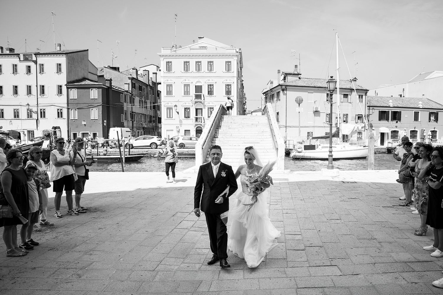 Wedding party walks across a scenic Venice plaza on a bright day.