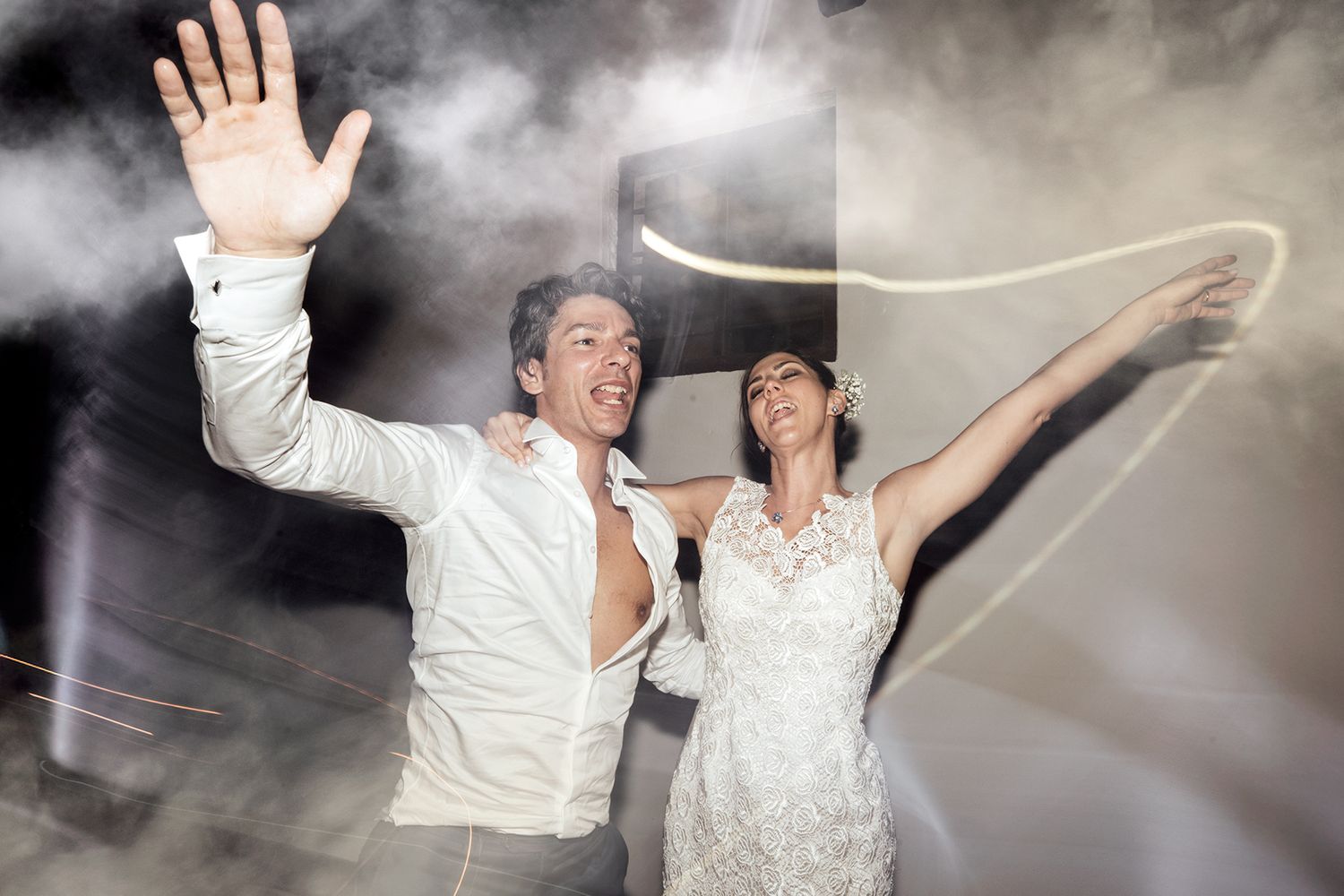 Wedding couple dancing energetically at their reception with dramatic lighting and smoke effects.