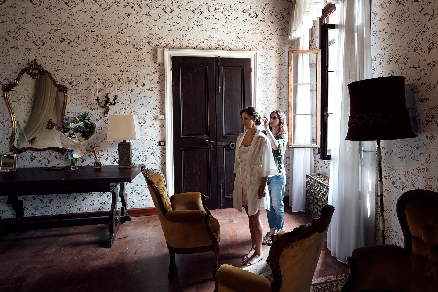 A vintage room with floral wallpaper, wooden furniture, and natural light streaming through windows.