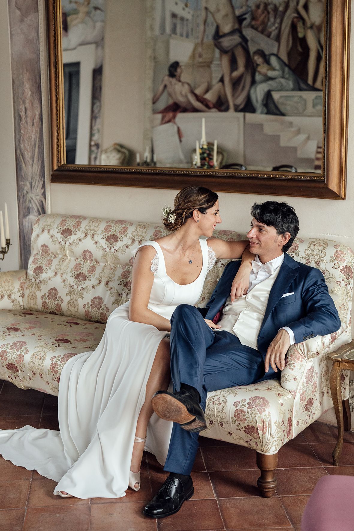 Wedding couple relaxing on vintage floral sofa in elegant indoor setting.