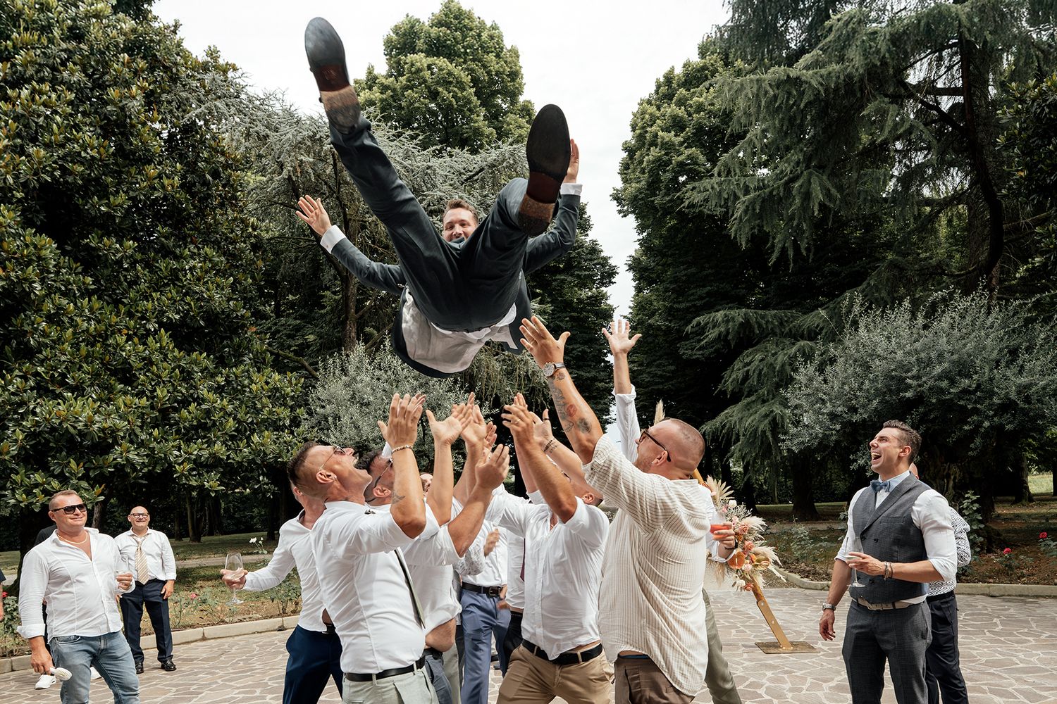 Wedding party celebrates joyfully outdoors with arms raised in a candid group shot.